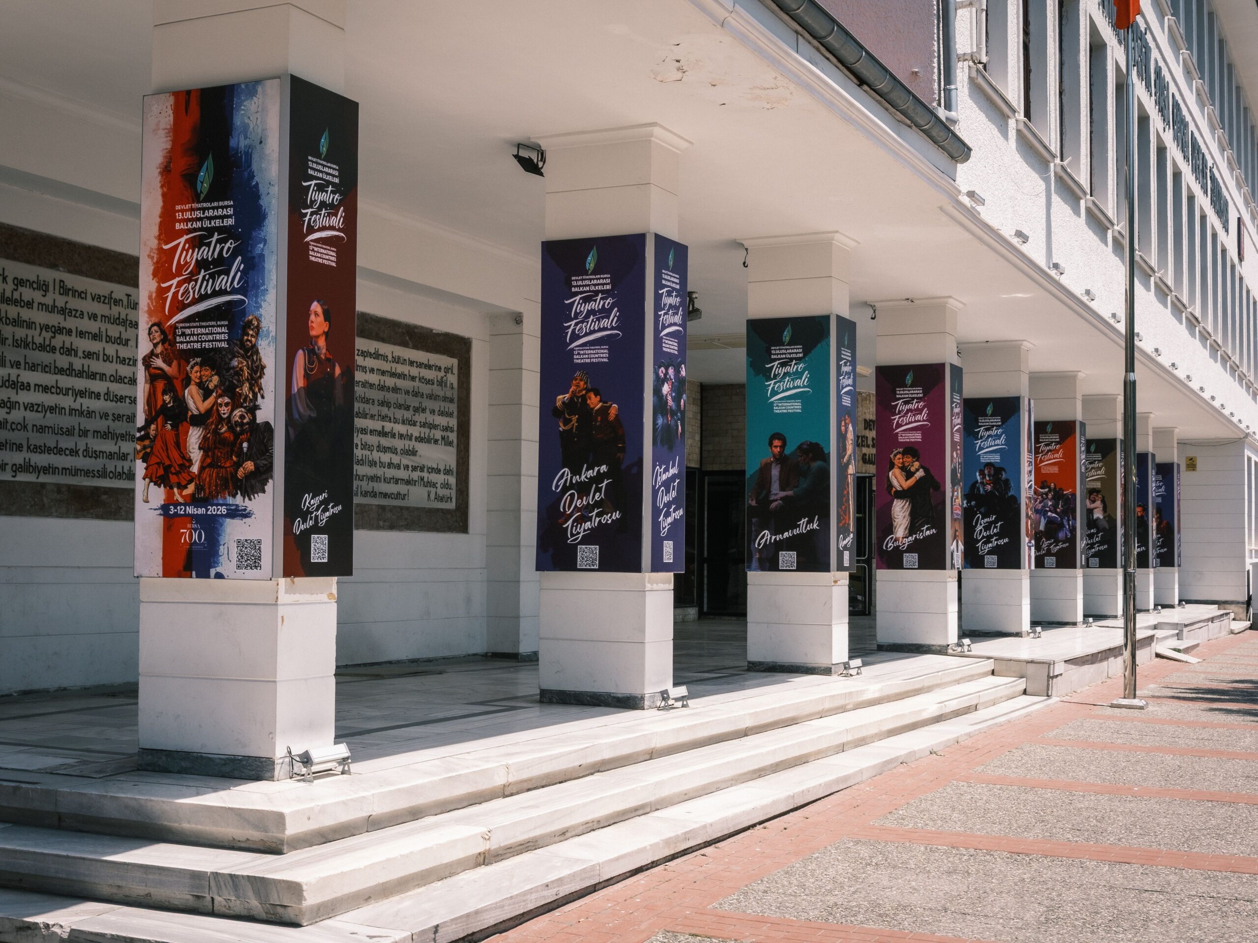 Colorful theatre festival posters on building columns outdoors in daylight.